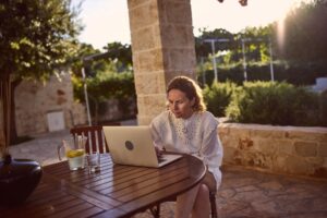 Woman Working Remotely on Laptop Outdoors at Sunny Mediterranean Terrace During Summer Afternoon